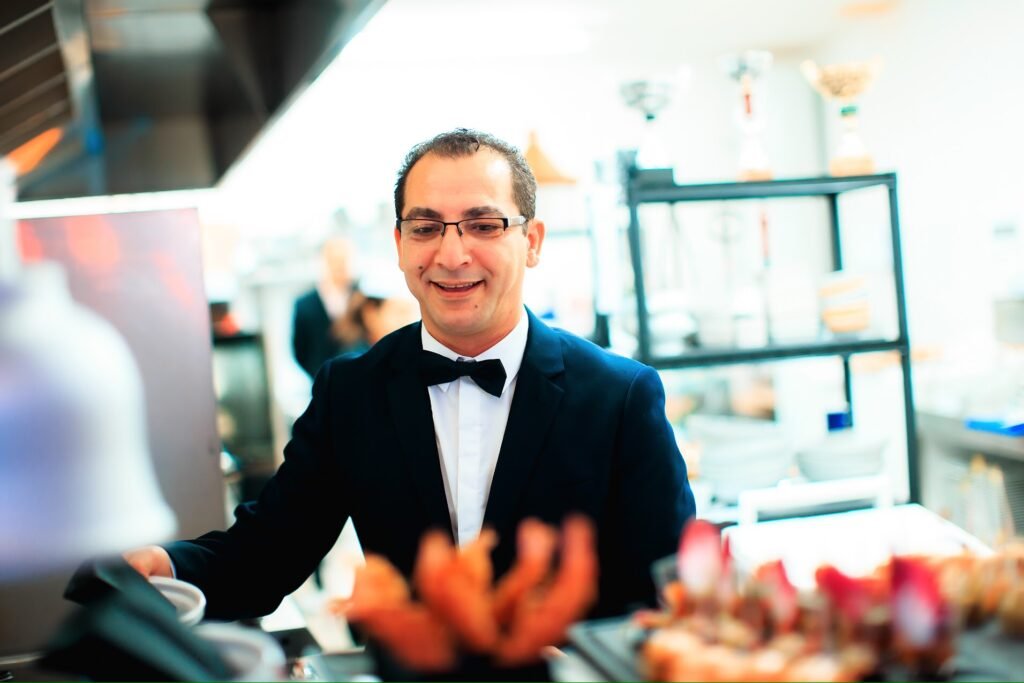 Chef Salah en costume et nœud papillon dans la cuisine de son restaurant marocain et méditerranéen à Cavaillon.